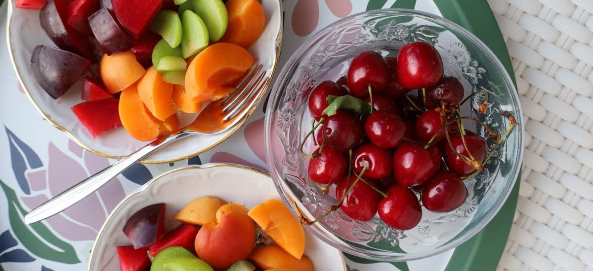 Vibrant mix of fresh summer fruits in decorative bowls on a floral patterned tray.