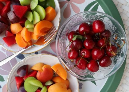 Vibrant mix of fresh summer fruits in decorative bowls on a floral patterned tray.
