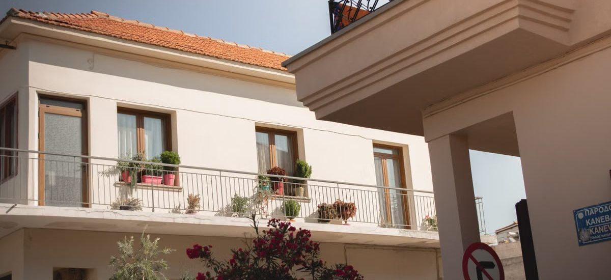 Traditional Greek house facade with potted plants and balcony details.